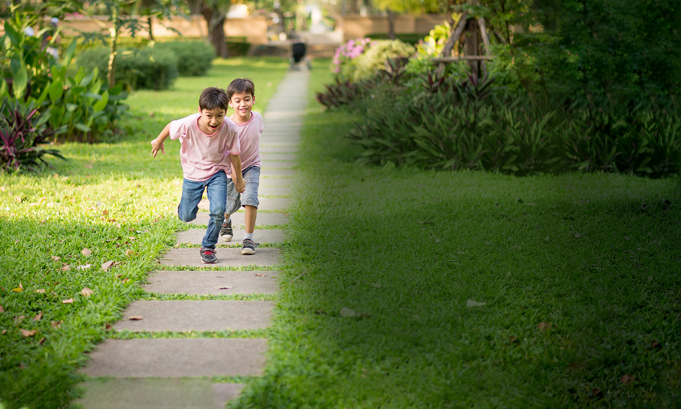 Two children running in a neighborhood with smiles on their faces